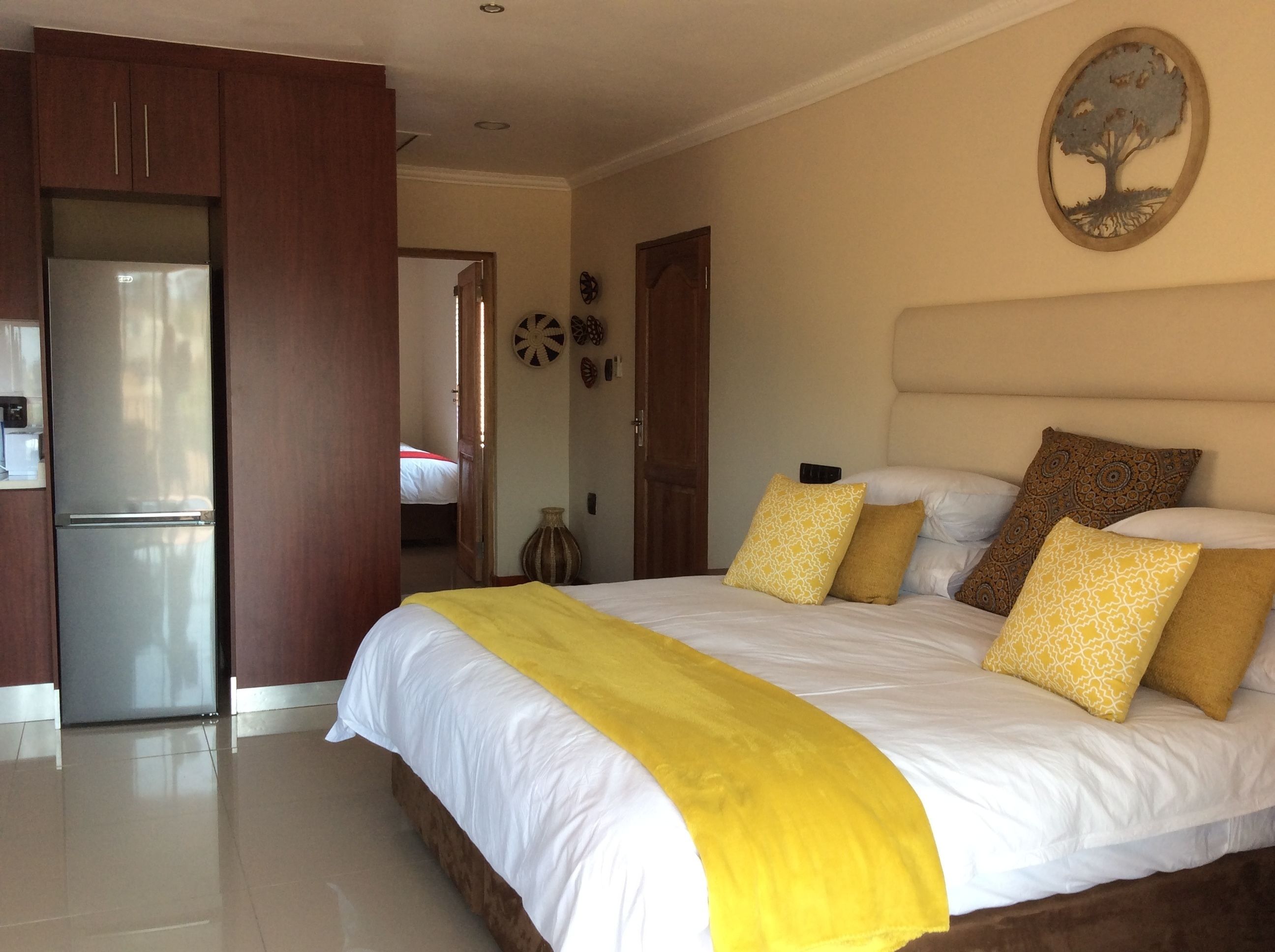 A bedroom with a bed, pillows, a nightstand, a wall clock, and a door leading to another room.