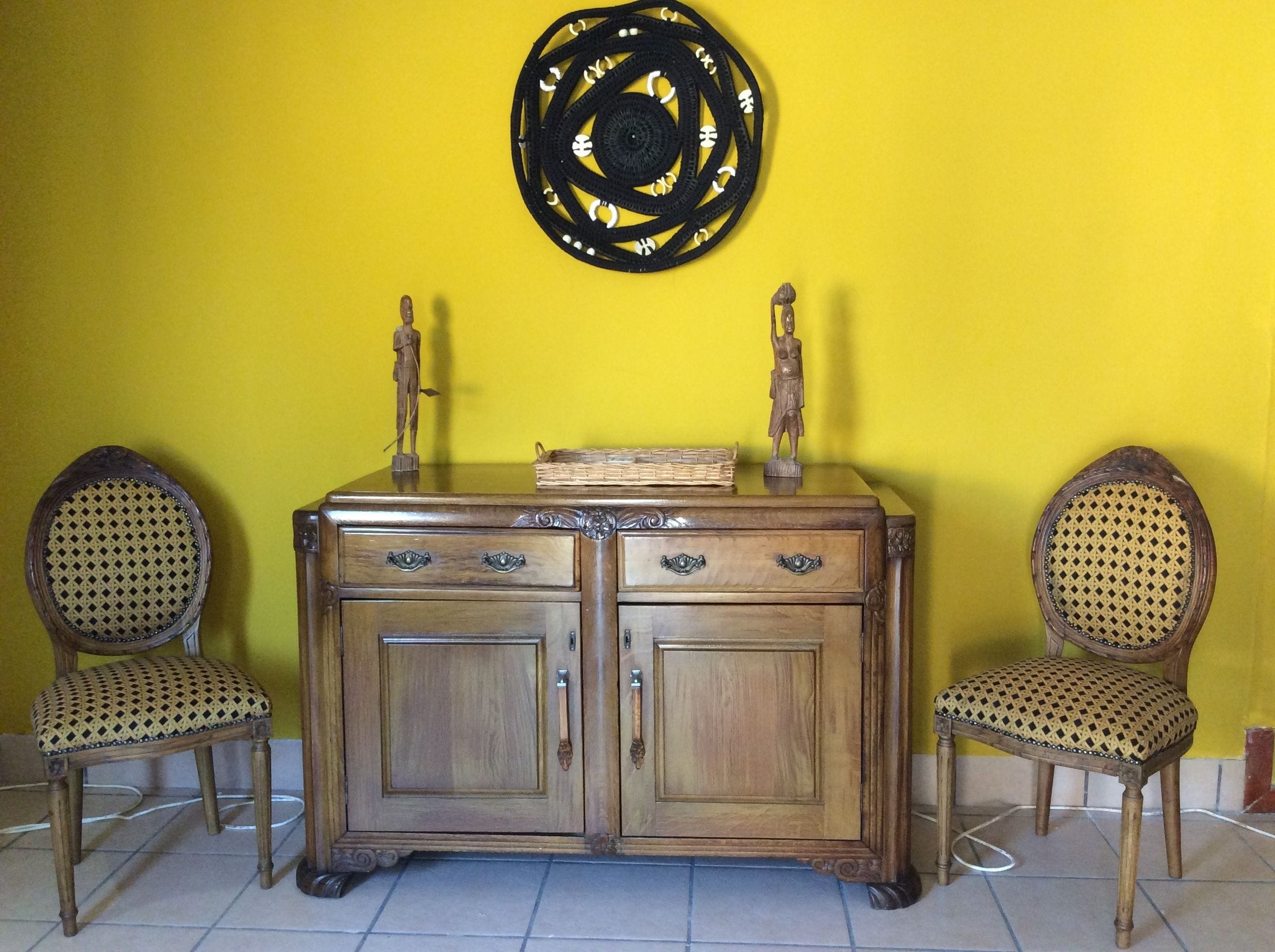 Un mueble de madera con dos cajones y un estante, flanqueado por dos sillas de mimbre con asiento y respaldo tejido.