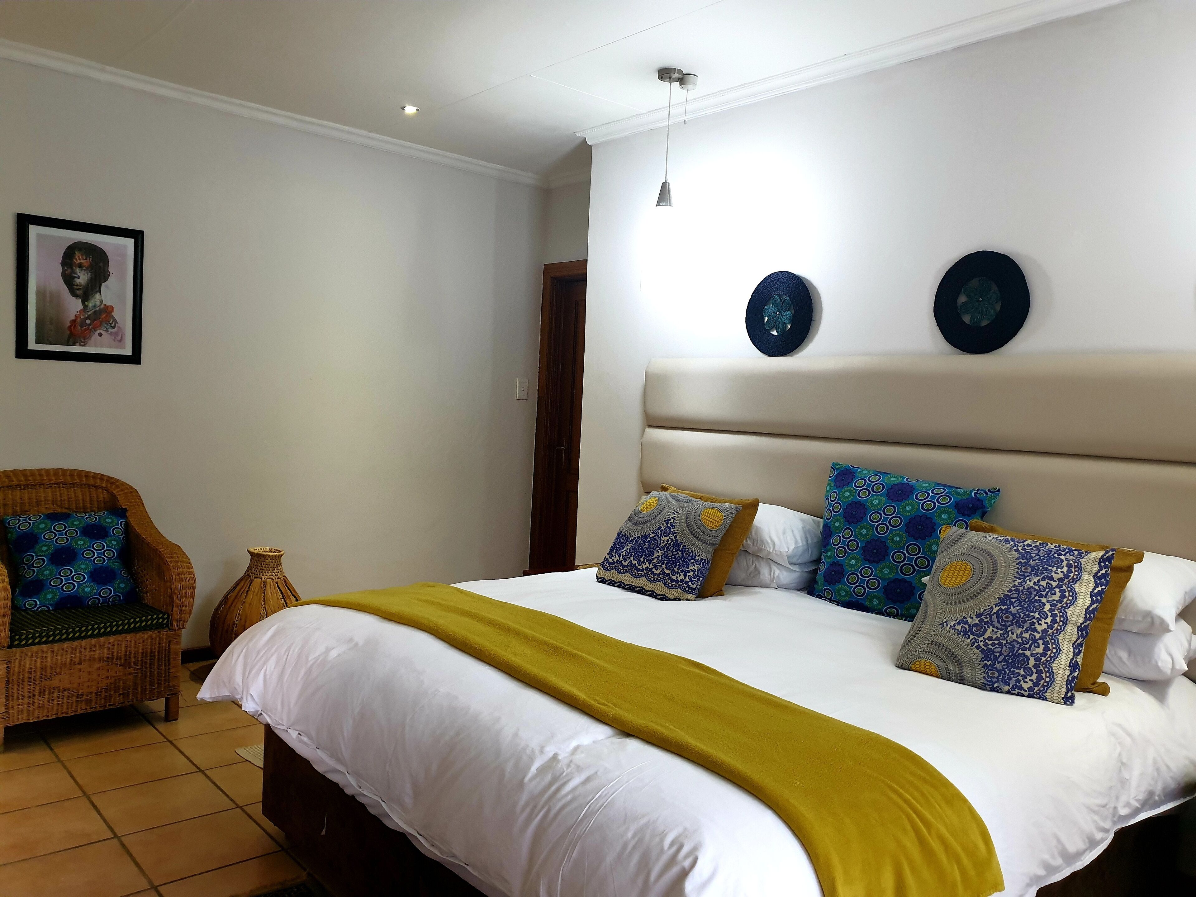 Un dormitorio con una cama grande, una silla de mimbre y una mesita.
