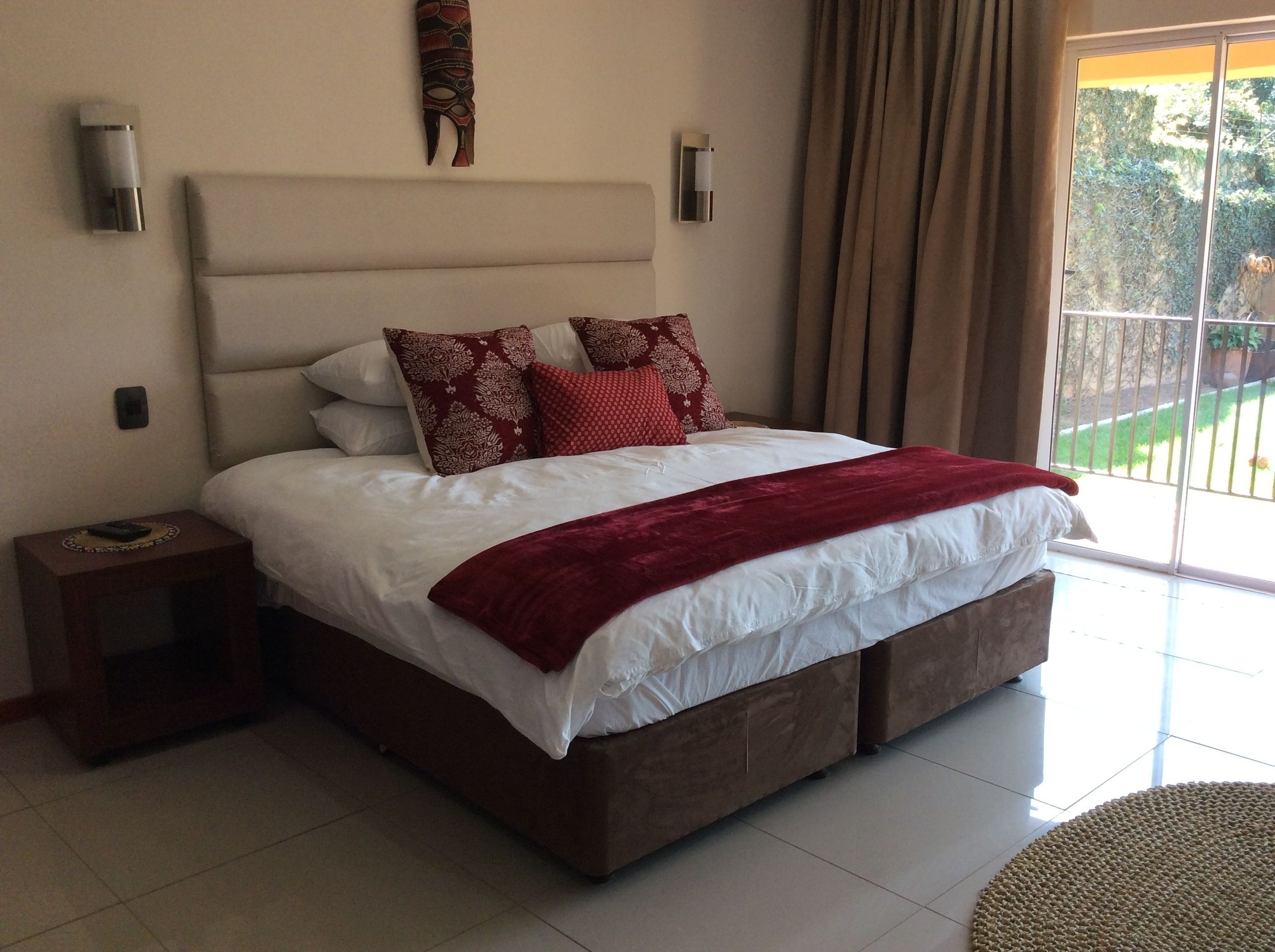 A bedroom with a large bed, a nightstand, a wall-mounted light, and a view of the outdoors through a sliding door.