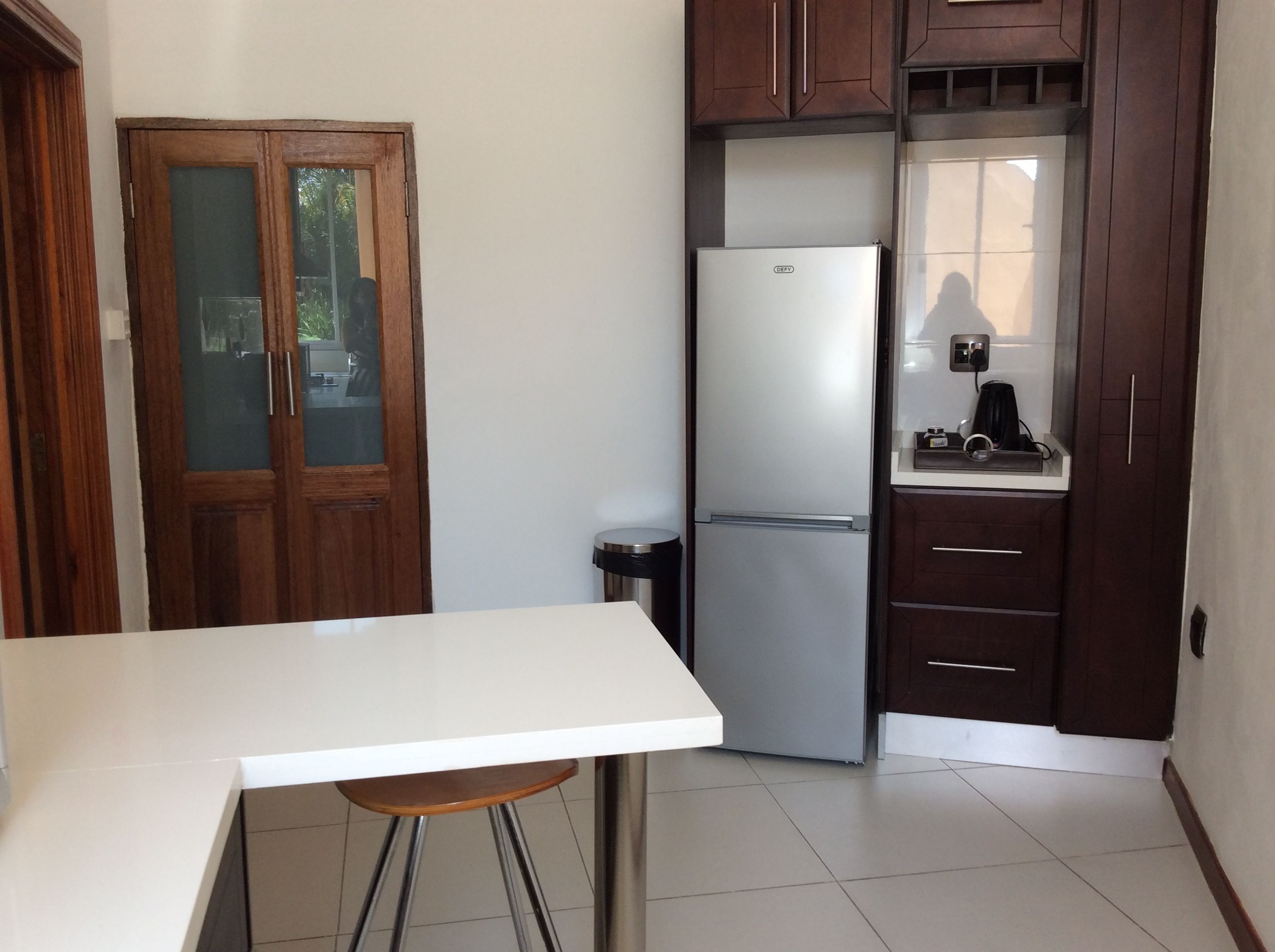 A kitchen with a white countertop, a stainless steel refrigerator, wooden cabinets, and a door with glass panels.