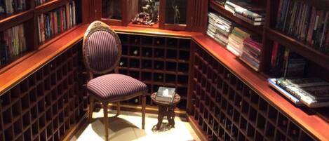 A library with bookshelves, a chair, a small table, and a patterned rug.