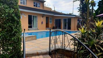 Un immobile residenziale con piscina, una scala che conduce a un patio e una casa ampia con porte scorrevoli in vetro.