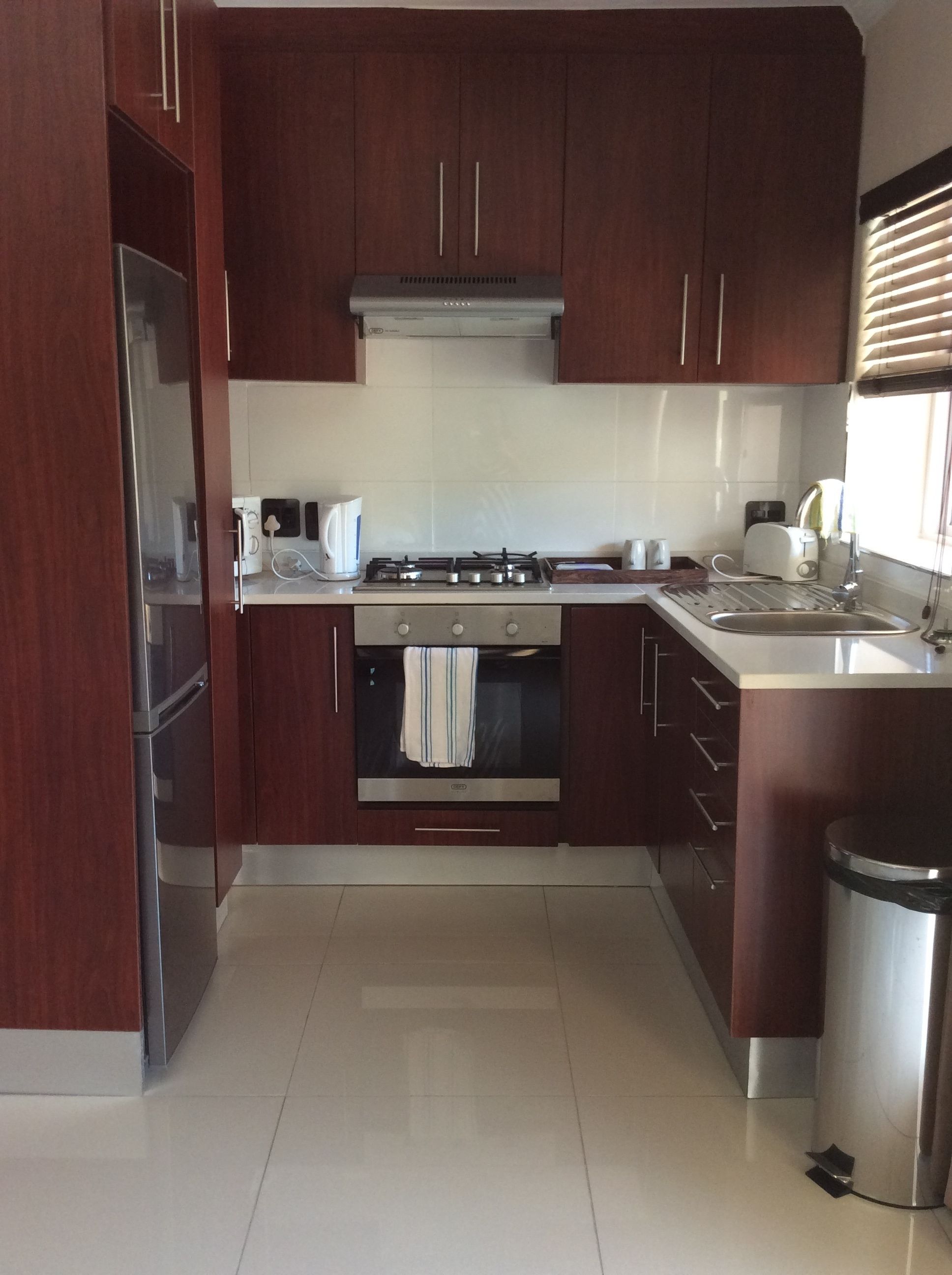 Una cocina compacta con armarios de madera oscura, una estufa de acero inoxidable, horno empotrado, un lavamanos y un cesto de basura.