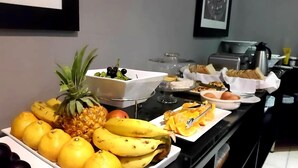 Un bufé con frutas como plátanos, limones y piña, y diversos platos que incluyen pan y huevos.