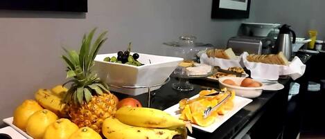 A buffet with fruits like bananas, lemons, and pineapple, and various dishes including bread and eggs.