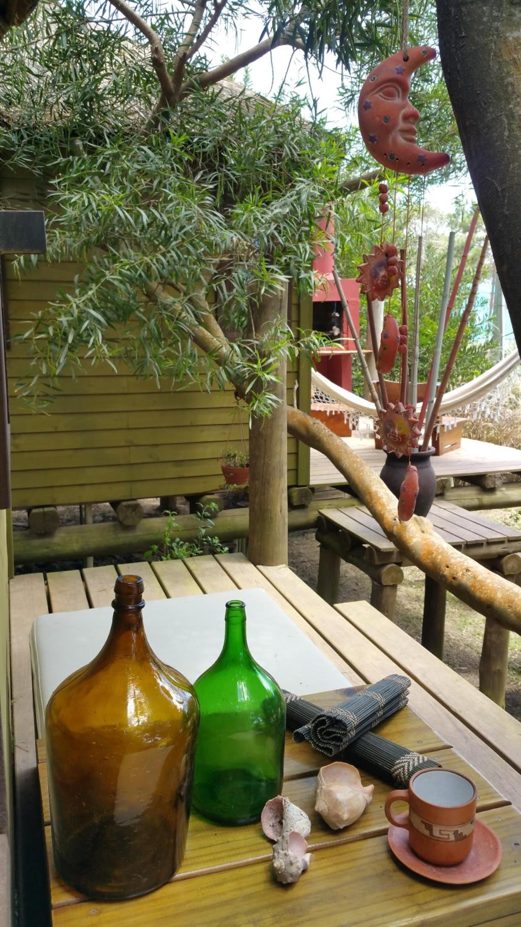 Uma mesa de madeira com uma garrafa, uma garrafa verde, um tapete enrolado, uma concha e uma chávena sobre um banco de madeira.