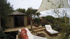 Une terrasse en bois avec deux chaises longues et un espace salon abrité.