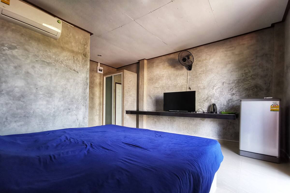 A room with a bed, a flat-screen TV, a small refrigerator, and a ceiling fan.