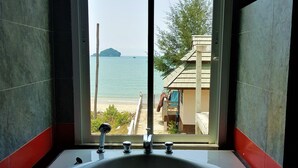 A bathroom with a large bathtub and a view of the sea through a sliding door. - Sea Smile Resort (Prachuap Khiri Khan)