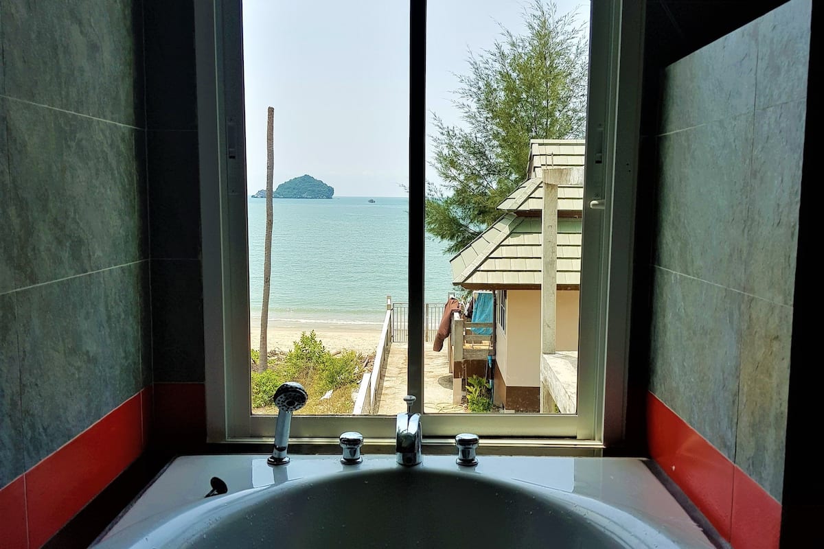 A bathroom with a large bathtub and a view of the sea through a sliding door.