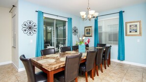 A dining room with a marble table, dark chairs, a chandelier, and teal curtains. - Paradise Palms #3 - 6 Bed 5 Baths Villa (Kissimmee)
