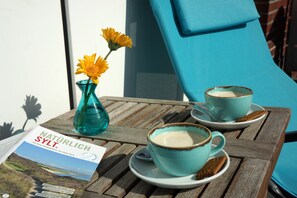 A wooden table with a book titled "Naturlich SÜLT." and two cups of coffee on saucers. - Hotel am Südwäldchen (Sylt)