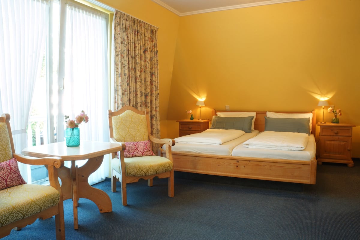 A hotel room with a bed, two chairs, a table, and a lamp.