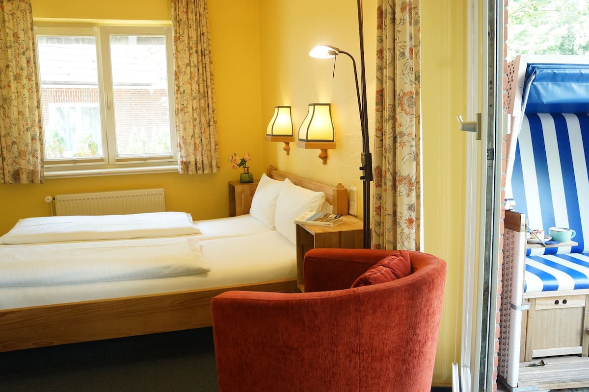 A hotel room with a bed, a red armchair, a nightstand with a lamp, and a window with curtains.