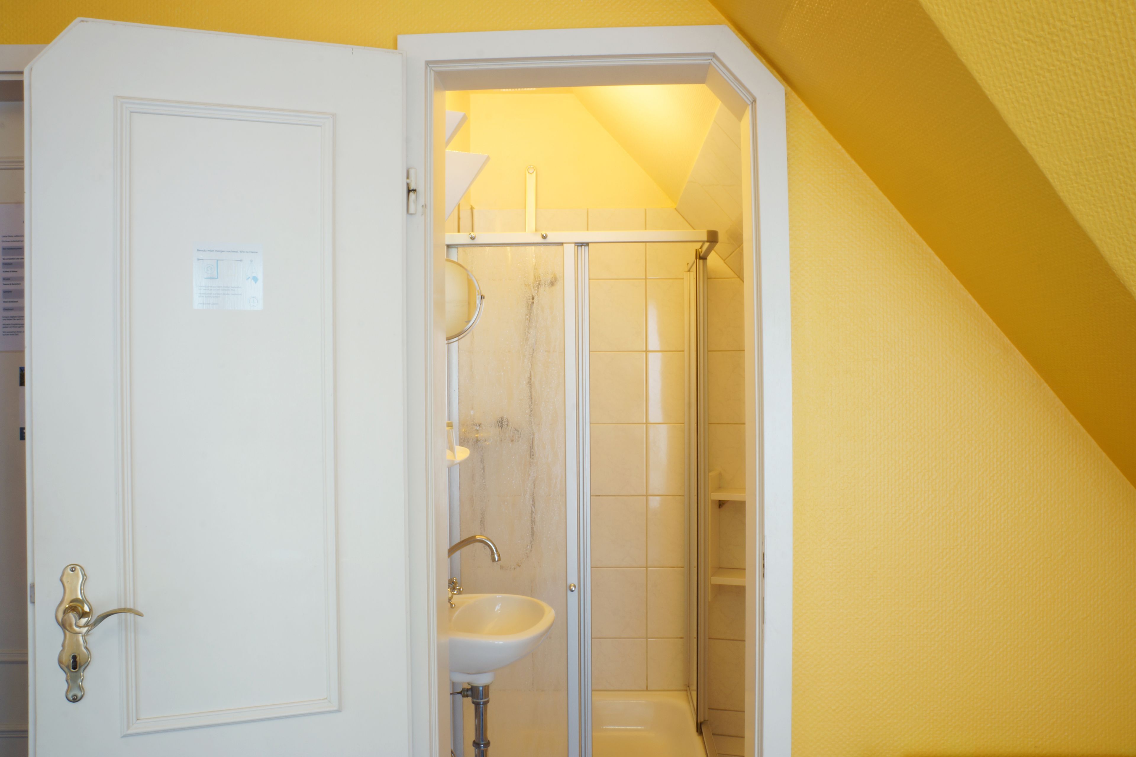 A small, enclosed bathroom with a white door, a sink, and a shower.