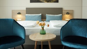 A hotel room with a bed, two chairs, a round table, and a painting above the bed. - Hotel am Südwäldchen (Sylt)
