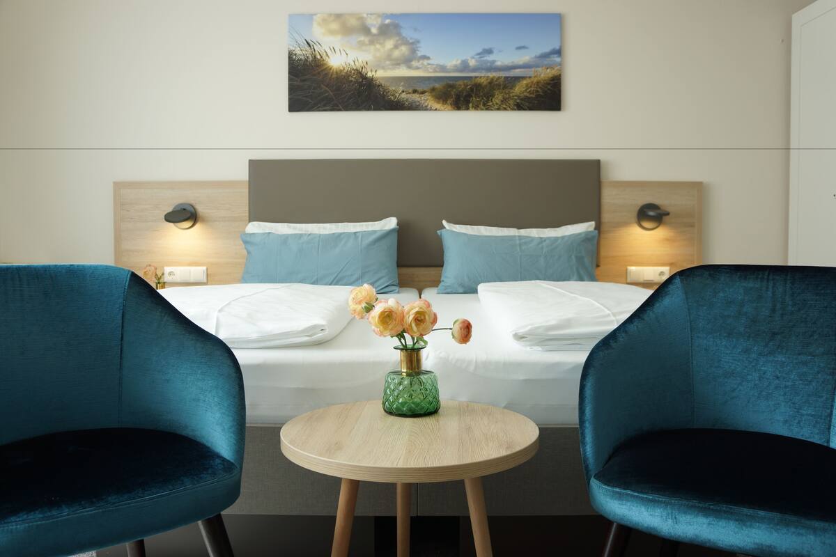 A hotel room with a bed, two chairs, a round table, and a painting above the bed.