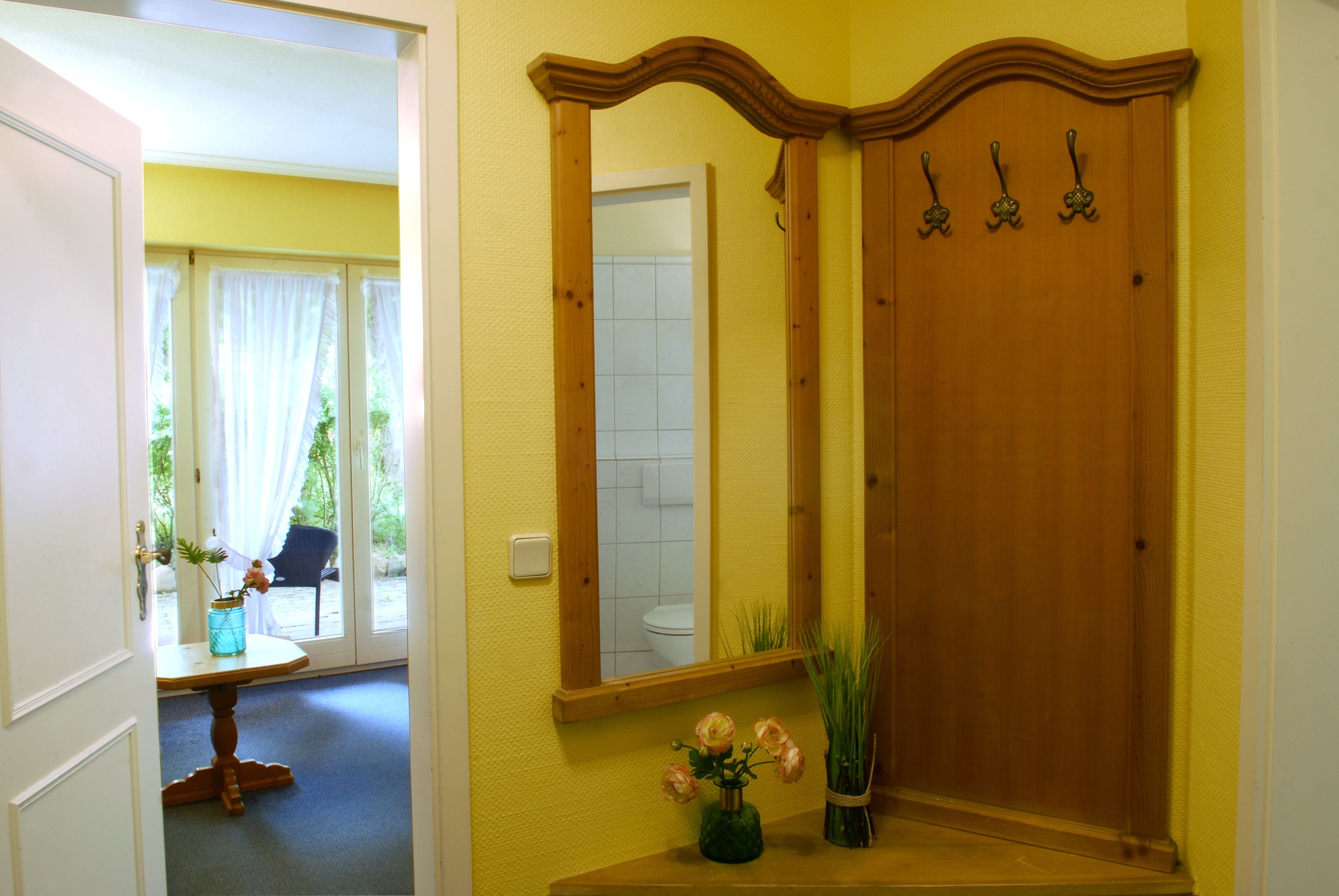 Een badkamer met een houten wastafelmeubel, een spiegel en een deur met haakjes.