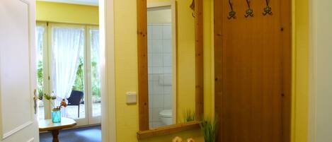 Een badkamer met een houten wastafelmeubel, een spiegel en een deur met haakjes.