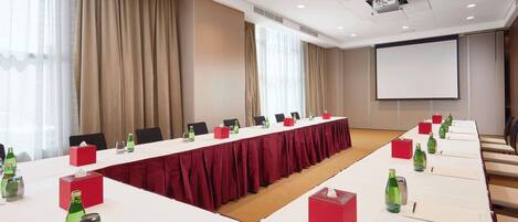 Et mødelokale med et langt bord, stole og et projektorskærm.