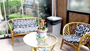 Un balcon agrémenté de meubles en osier, d’une table en verre et d’une plante en pot.