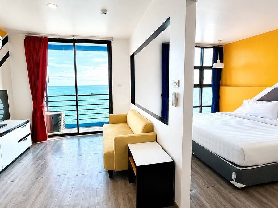 Habitación de hotel con cama, escritorio, silla, televisor y vista al mar.