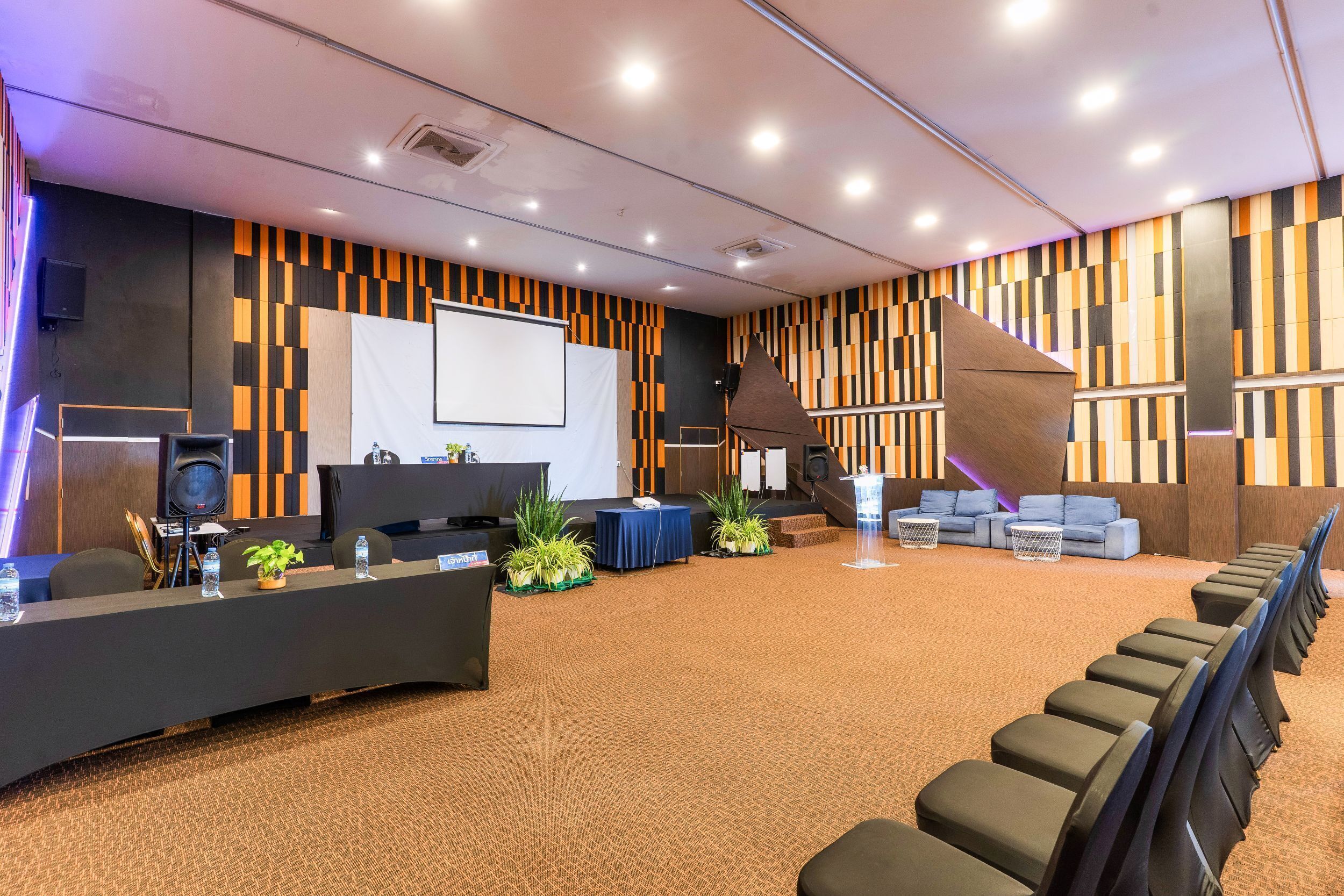 Un salón de conferencias con escenario, una pantalla grande, un atril y filas de sillas.
