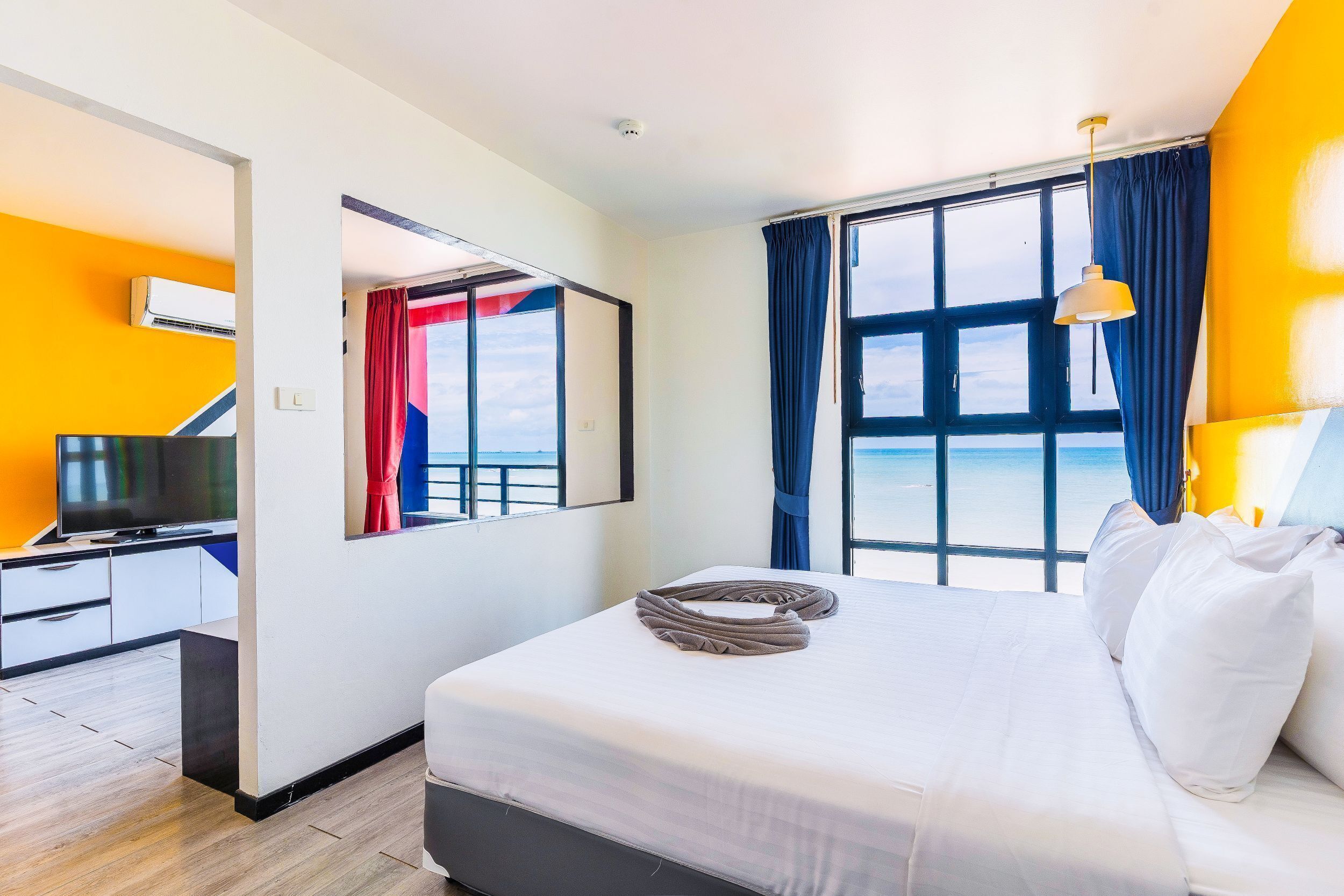 A hotel room with a bed, a television, a desk, and a window with a view of the sea.