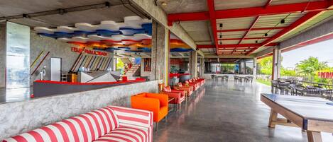 A spacious indoor area with a long counter, seating with striped cushions, and a ceiling with colorful wave patterns.