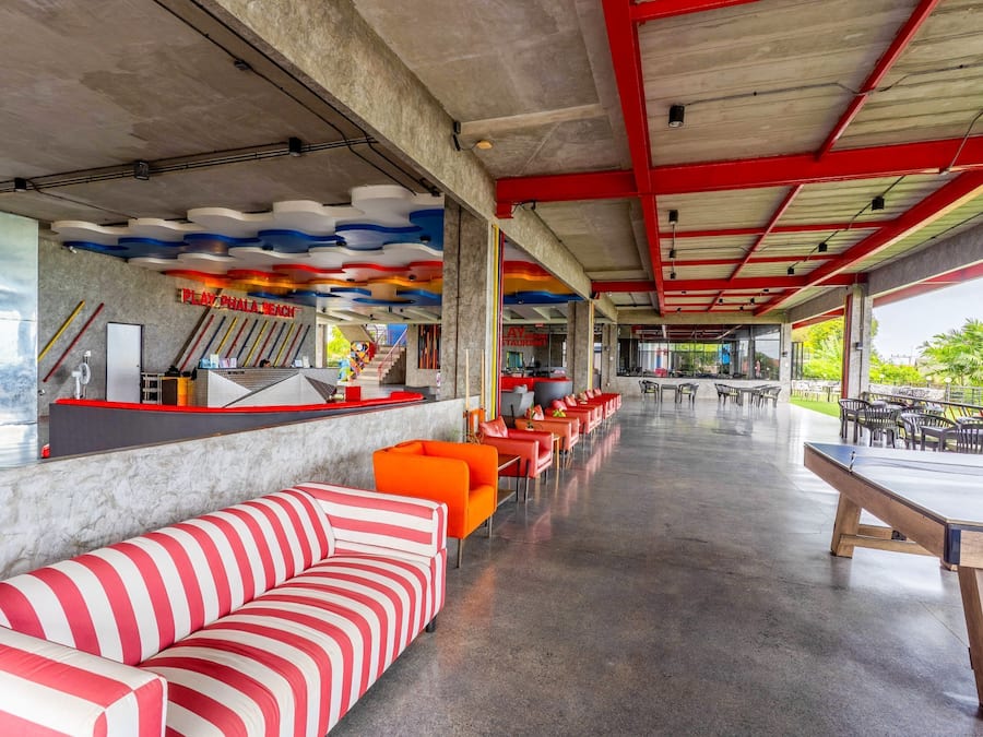 A spacious indoor area with a long counter, seating with striped cushions, and a ceiling with colorful wave patterns.