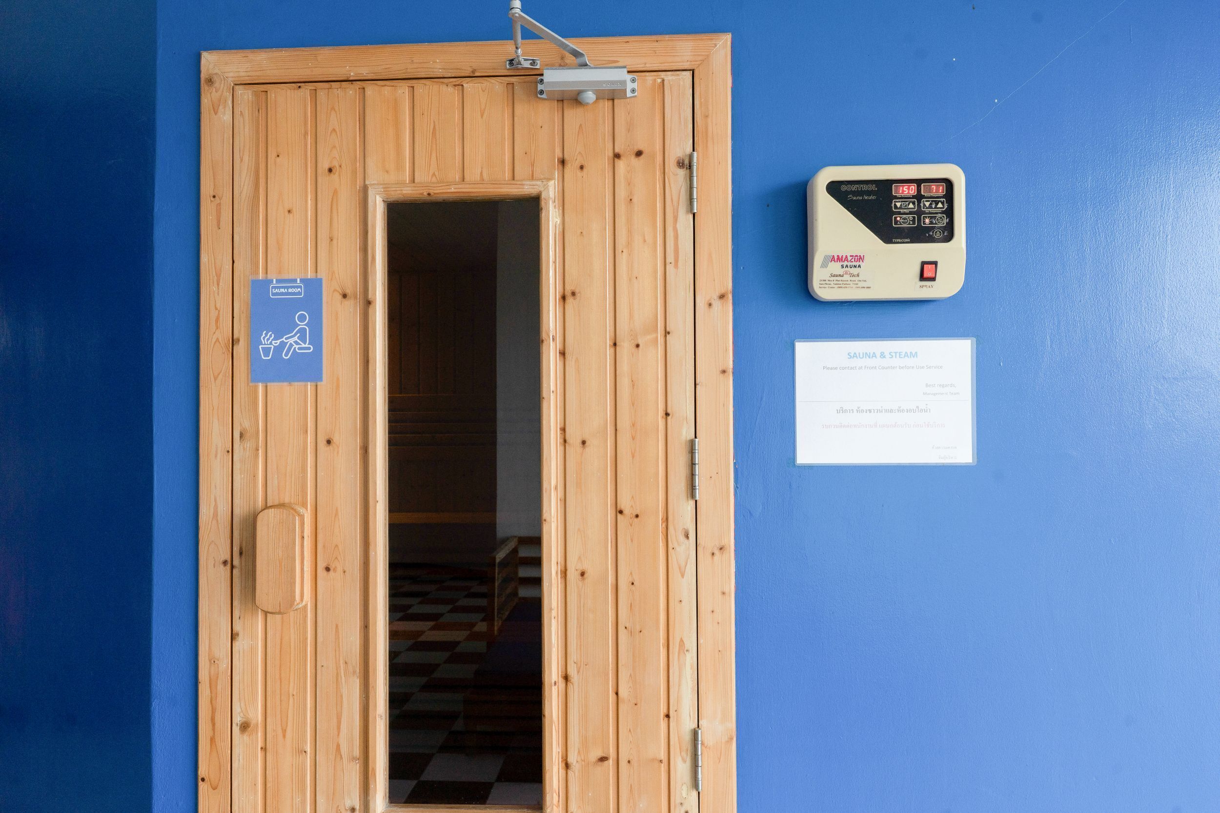 A wooden door with a sauna sign, a sauna control panel, and a service card on a blue wall.