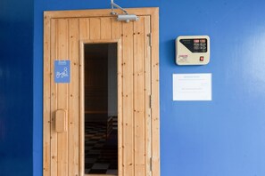 A wooden door with a sauna sign, a sauna control panel, and a service card on a blue wall. - Play Phala Beach Rayong (Ban Chang)