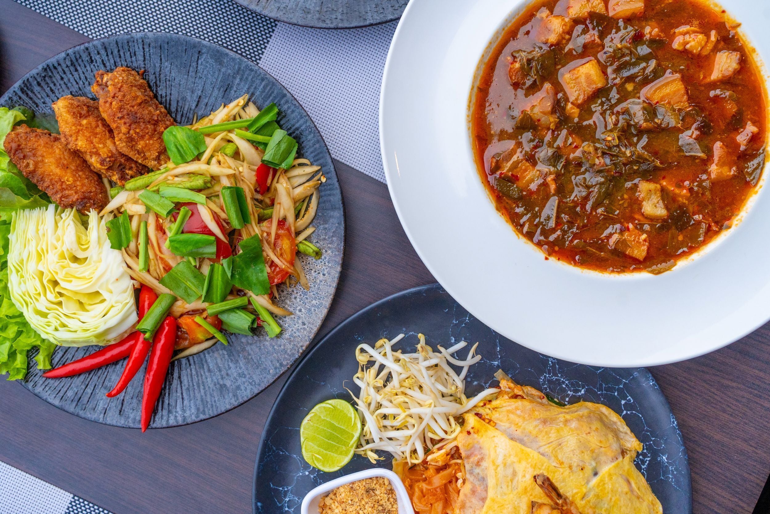 A table with a variety of dishes including a bowl of soup, a plate of fried items, a salad, and a plate with a lime wedge.