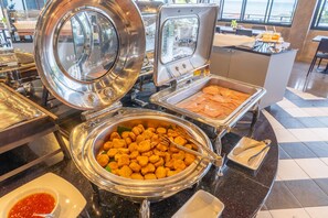 A buffet setup with various food items in metal containers, including a bowl of orange-colored appetizers and a tray of food covered with foil. - Play Phala Beach Rayong (Ban Chang)
