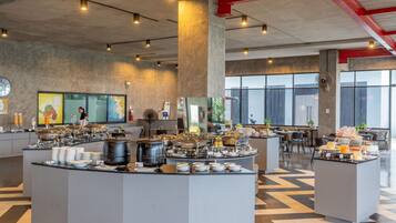 Un moderno comedor de desayuno tipo buffet con varias estaciones de comida, un reloj y obras de arte en las paredes.