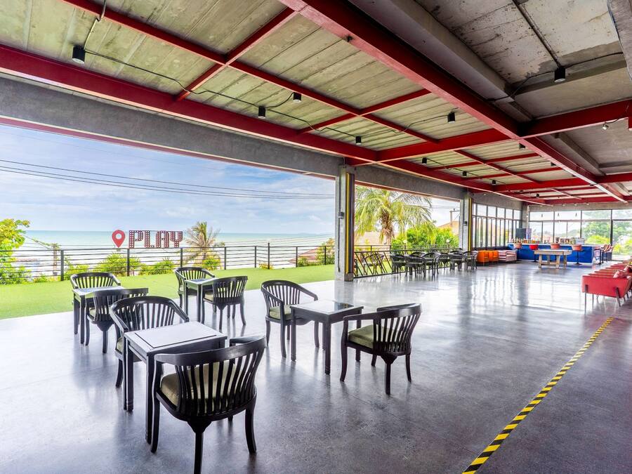 An outdoor seating area with tables and chairs, a view of the ocean, and a sign that reads 'PLAY'.