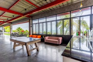 Amplio espacio interior con mesa de ping pong, asientos y ventanas grandes que ofrecen vistas al mar.