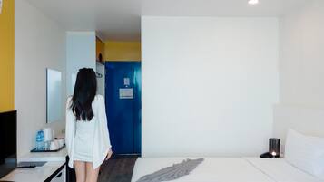 A hotel room with a bed, a desk with a chair, a mirror, and a blue door.