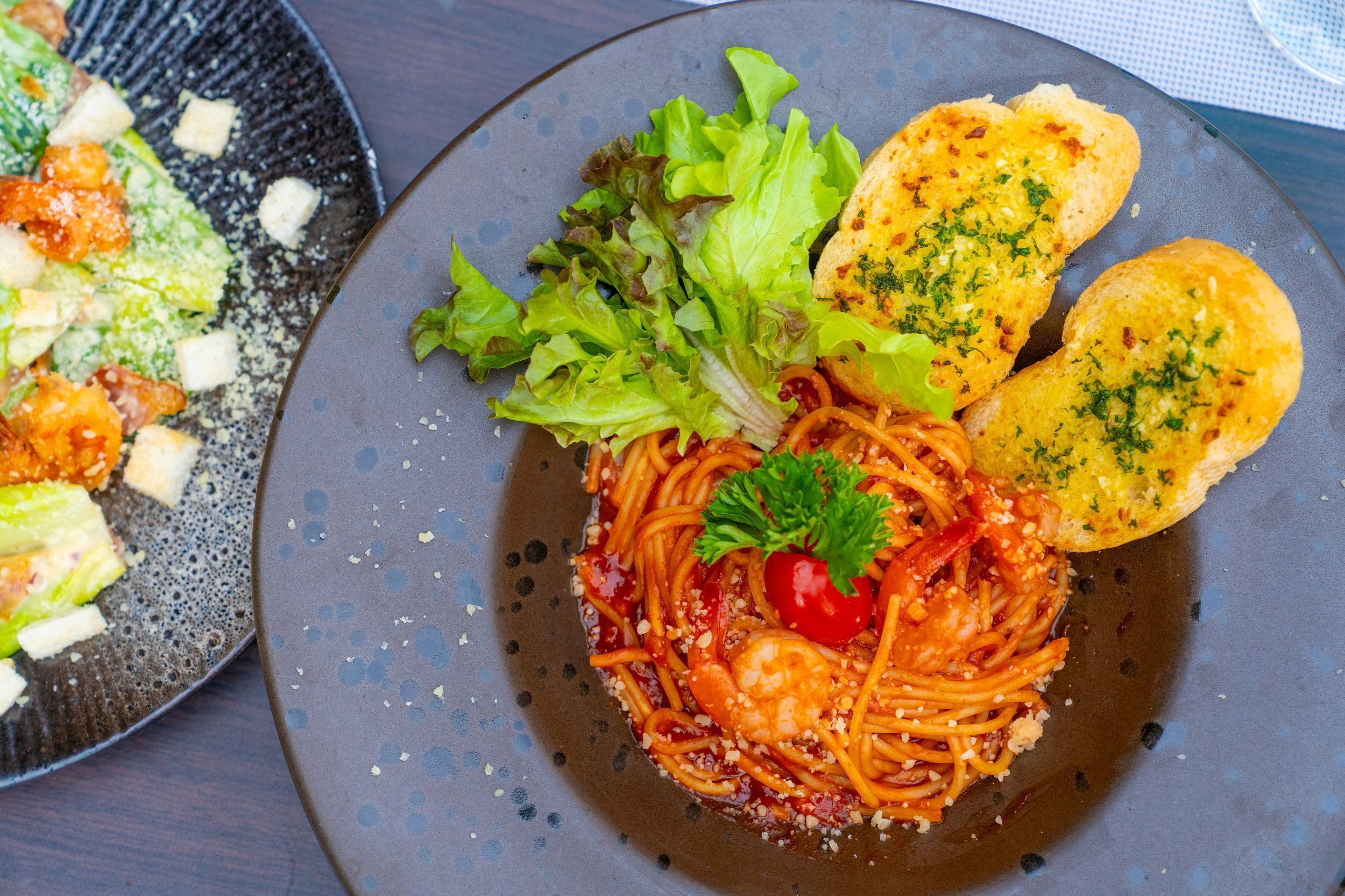 Une assiette de spaghettis garnie de tomates cerises et de persil, accompagnée d’une salade et de pain grillé.