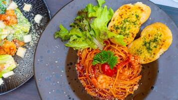 Un plato de espagueti con tomate cereza y perejil, acompañado de una ensalada y pan tostado.