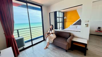 A hotel room with a large sliding glass door to the sea, a bed with a headboard, and a sofa.