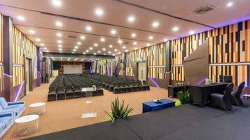 Un salón de conferencias con filas de sillas, un escenario y una zona de estar con mesas y sillas.