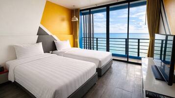 A hotel room with two beds, a TV, and a large window with a view of the sea.