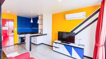 A compact living space with a kitchenette, a flat-screen TV, and a red sofa.
