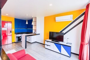 Un espacio habitable compacto con kitchenette, un televisor de pantalla plana y un sofá rojo.