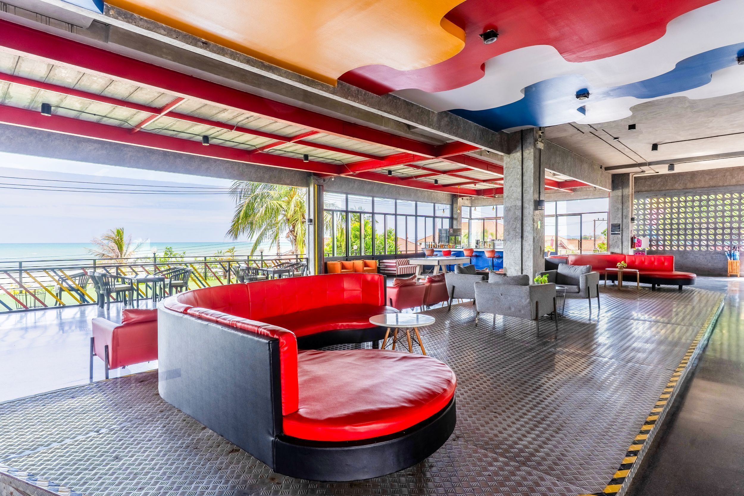 A modern lounge area with a view of the ocean, featuring red and black seating, a patterned floor, and a ceiling with a colorful design.