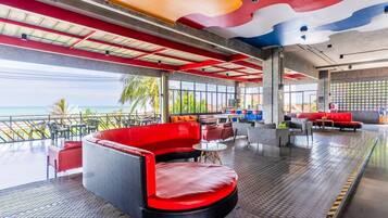 A modern lounge area with a view of the ocean, featuring red and black seating, a patterned floor, and a ceiling with a colorful design.