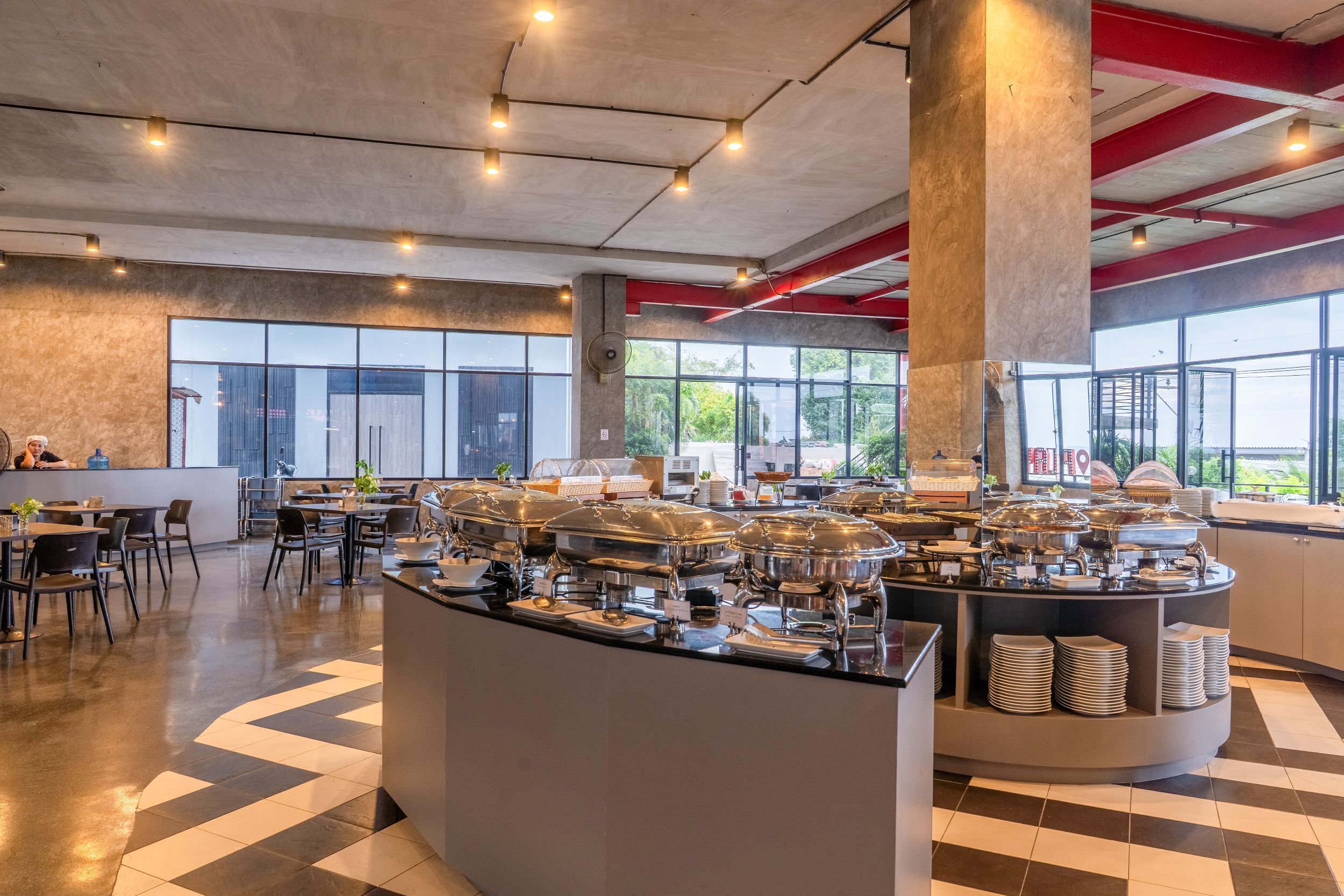 A modern cafe with a buffet setup, large windows, and a check-in counter.