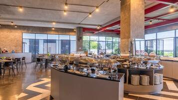 A modern cafe with a buffet setup, large windows, and a check-in counter.